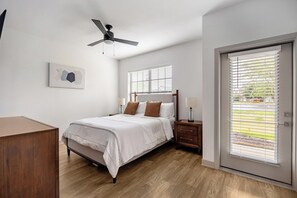 Un dormitorio con cama, mesitas de noche, ventilador de techo, ventana con persianas y una puerta.