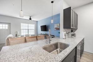 A modern kitchen with a granite countertop, stainless steel sink, and black cabinets. - Landing | Stylish 1BD, Clubhouse, Gym (McCordsville)