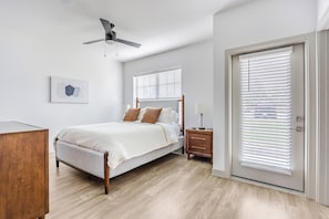 A bedroom with a bed, bedside table, lamp, ceiling fan, and a door with blinds. - Landing | Stylish 1BD, Clubhouse, Gym (McCordsville)