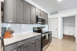 A modern kitchen with grey cabinets, a stainless steel microwave, an oven, and a granite countertop. - Landing | Stylish 1BD, Clubhouse, Gym (McCordsville)