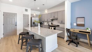 Una cocina moderna con una isla central, taburetes de bar, una zona de comedor con escritorio y una pared azul decorativa.