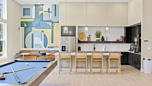 Una cocina moderna con una isla central, taburetes de bar y una mesa de billar en una sala de estar.
