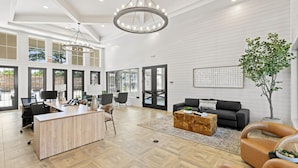 Amplia sala de estar con un escritorio grande de madera, un sofá negro y una mesa de centro. Varias ventanas ofrecen luz natural y vistas al exterior.