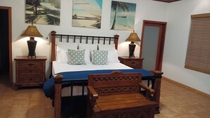 Une chambre à coucher comprenant un lit, deux tables de chevet, une chaise en bois et trois tableaux accrochés au mur.