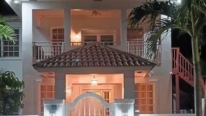 Une maison à deux étages, avec un toit en tuiles, une entrée fermée par un portail et un escalier situé sur le côté droit.
