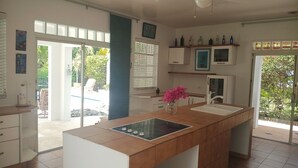 Une cuisine moderne dotée d’un îlot central, de meubles blancs, d’un ventilateur de plafond et offrant une vue sur l’espace extérieur.