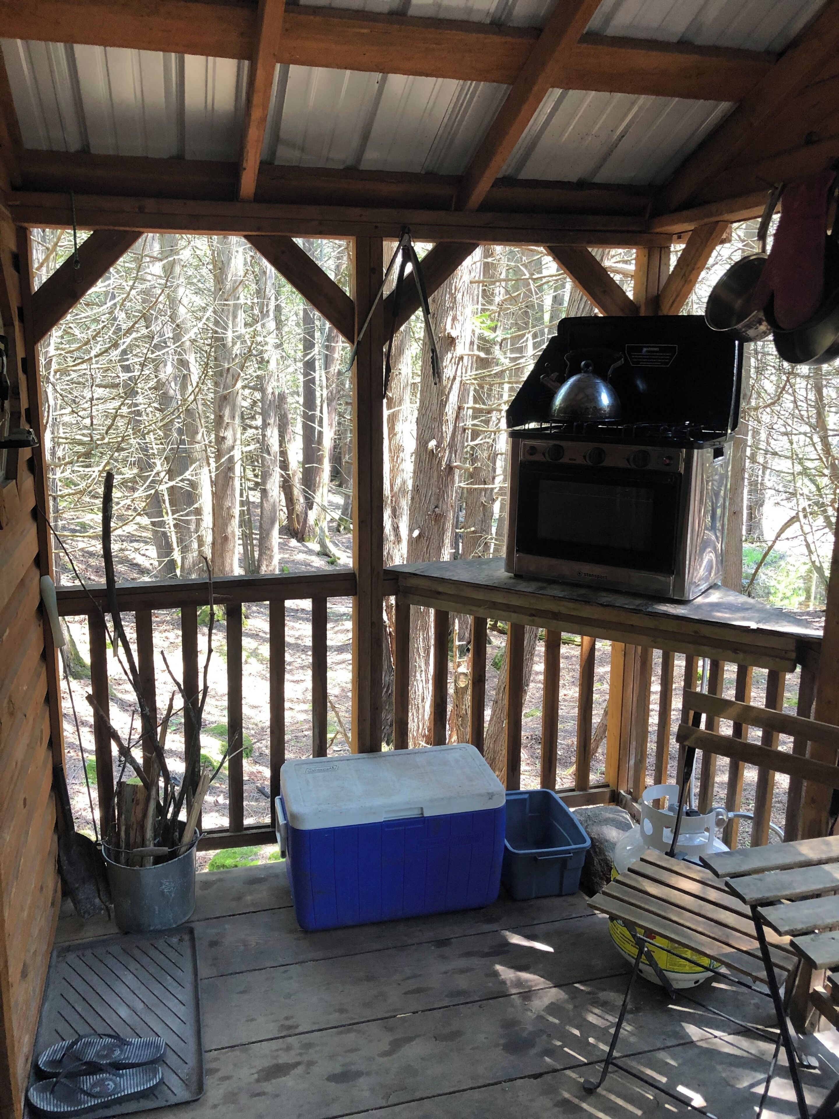 A covered outdoor area with a grill, a cooler, and a table.