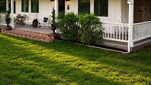 A two-story house with a covered porch, a brick chimney, and a well-maintained lawn.