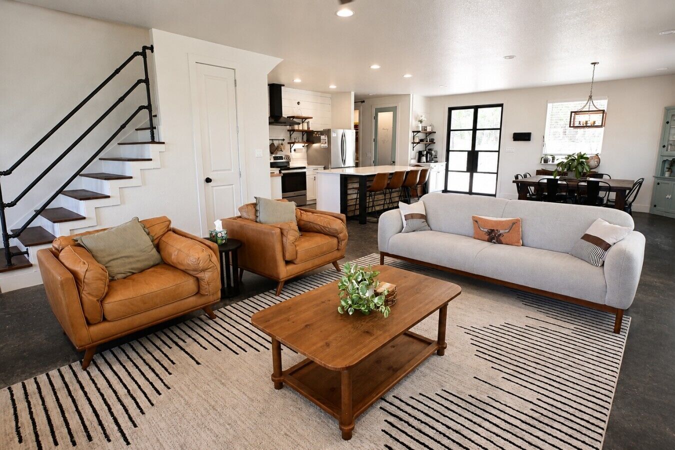 A modern living room with a sofa, two armchairs, a coffee table, and a staircase.