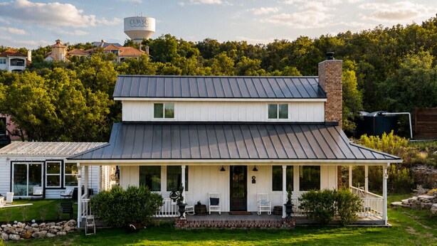 A two-story house with a covered porch, a water tank, and a well-maintained lawn.