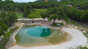 A natural pool surrounded by stone walls, trees, and a small bridge.