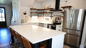 A modern kitchen with a central island, stainless steel appliances, and wooden shelves.