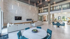 A spacious living area with a large white sofa, a round marble table with chairs, and pendant lighting. - Landing | Beautiful 1BD, Gym, Yoga Studio (Pooler)