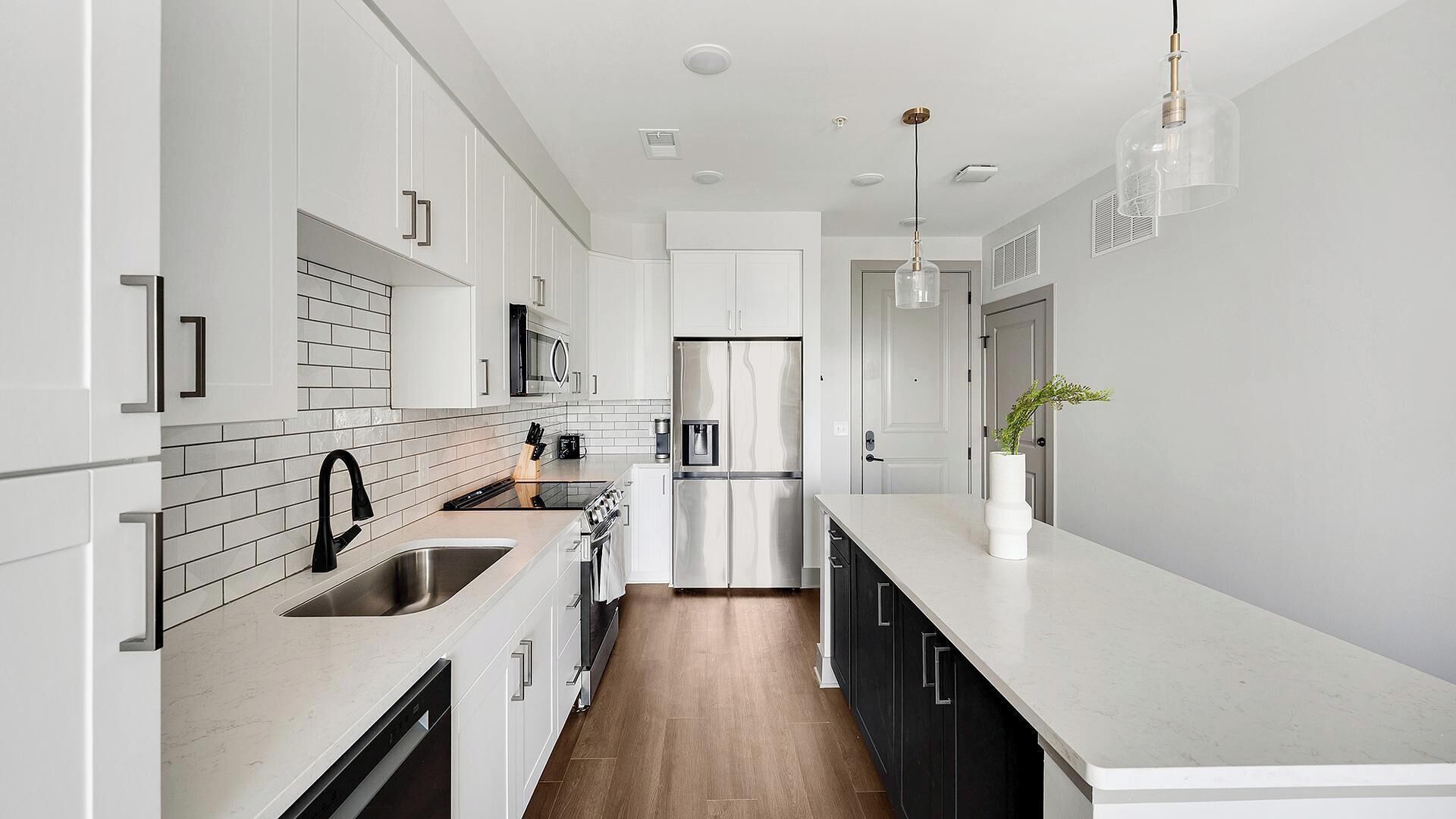 Una cocina moderna con armarios blancos, un refrigerador de acero inoxidable y piso de madera.