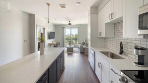 A modern kitchen with white cabinetry, a built-in oven, and a large window overlooking a cityscape. - Landing | Chic 1BD, Courtyard, Gym (Nashville)