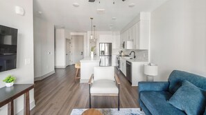 A modern living room with a sofa, a TV, and a dining area with a table and chairs. - Landing | Stylish 1BD, Courtyard, Yoga Studio (Nashville)