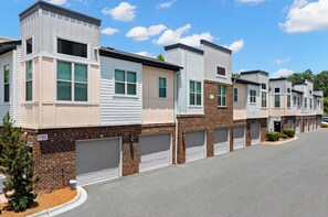 A row of modern townhouses with brick facades, white siding, and green shutters. Each unit has a garage. - Landing | Spectacular 2BD, Clubhouse, Gym (Charlotte)
