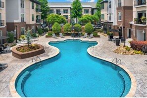 A swimming pool with a wavy design, surrounded by lounge chairs and potted plants. - Landing | Spectacular 2BD, Clubhouse, Gym (Charlotte)