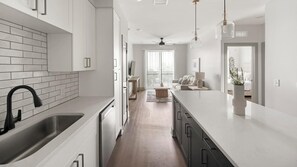 A modern kitchen with white cabinetry, a black faucet, and a wooden floor. - Landing | Modern 2BD, Yoga Studio, Gym (Nashville)