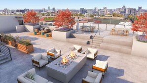 Eine Dachterrasse mit Sitzgelegenheiten im Freien, einem Feuerkorb und Blick auf die Stadt.
