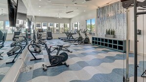 Une salle de sport moderne dotée de divers appareils d’exercice, de grandes fenêtres et d’un sol à motifs.