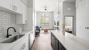 A modern kitchen with white cabinets, a black faucet, and a wooden floor. - Landing | Chic 1BD, Gym, Courtyard (Nashville)