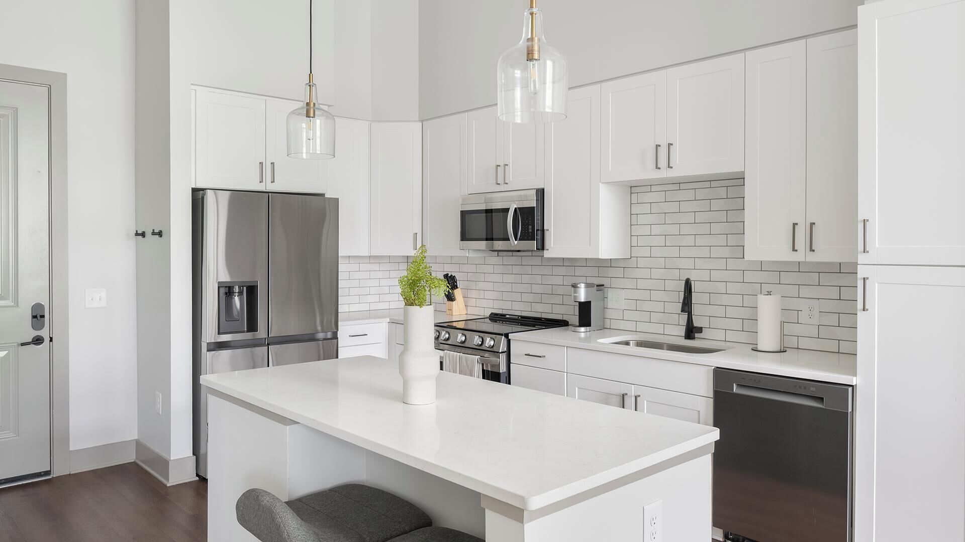 A modern kitchen with white cabinetry, stainless steel appliances, a central island, and pendant lighting.