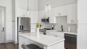 A modern kitchen with white cabinetry, stainless steel appliances, a central island, and pendant lighting. - Landing | Chic 1BD, Gym, Courtyard (Nashville)