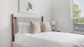 A bed with white bedding, a wooden headboard, and two patterned pillows. - Landing | Modern 1BD, Courtyard, Gym (Nashville)