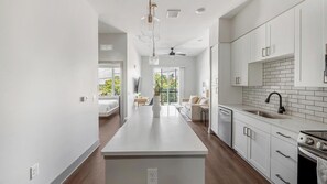 A modern kitchen with white cabinetry, a central island, and a view to a balcony. - Landing | Spectacular 1BD, Yoga Studio, Courtyard (Nashville)