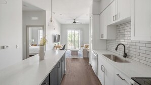 Une cuisine moderne avec des meubles blancs, un robinet noir et un coin repas comprenant un canapé et une table.
