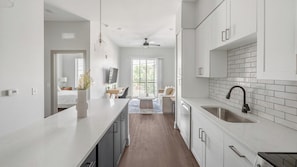 A modern kitchen with white cabinets, a black faucet, and a dining area with a sofa and table. - Landing | Spectacular 1BD, Yoga Studio, Courtyard (Nashville)