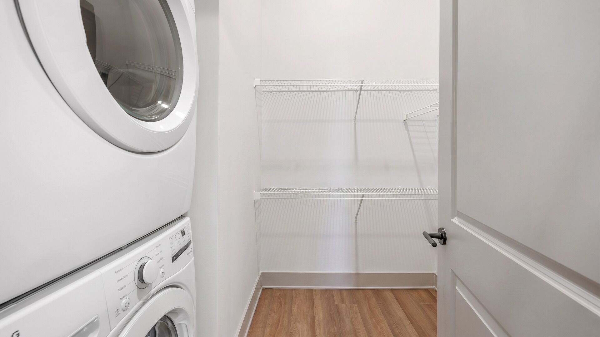 A laundry room with a front-loading washer and dryer, a metal drying rack, and a wooden floor.