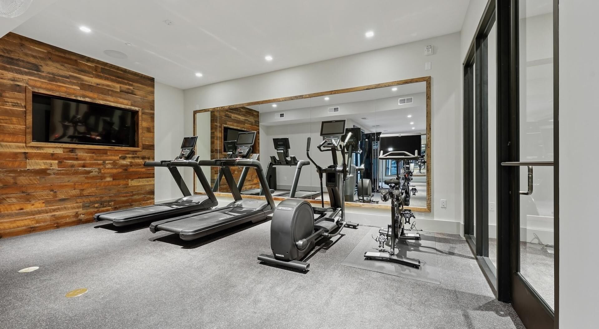 Une salle de sport équipée de tapis de course, d’un appareil elliptique et de vélos d’exercice, avec un mur en bois et un grand miroir.