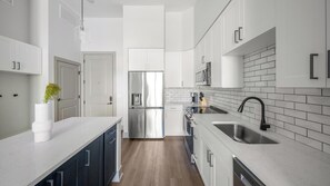 A modern kitchen with white cabinetry, stainless steel appliances, and a wooden floor. - Landing | Amazing 1BD, Gym, Courtyard (Nashville)