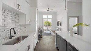 A modern kitchen with white cabinets, a black faucet, and a dining area with a sofa and table. - Landing | Spectacular 1BD, Gym, Courtyard (Nashville)