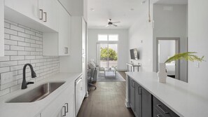 A modern kitchen with white cabinets, a black faucet, and a dining area with a sofa and table. - Landing | Amazing 1BD, Gym, Courtyard (Nashville)