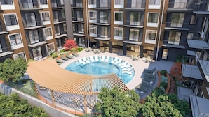 Un moderno edificio de apartamentos con un patio central que cuenta con piscina, sillones de descanso y mobiliario exterior.