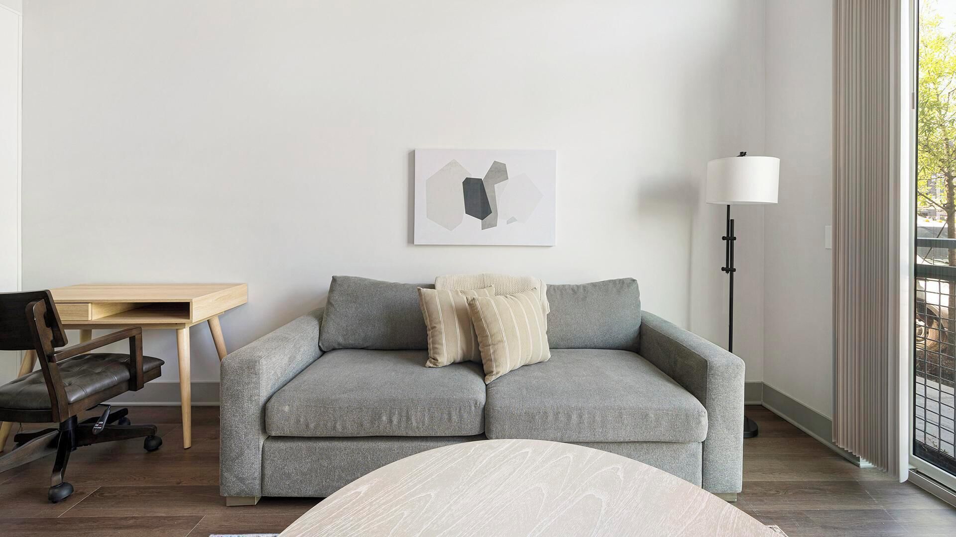 Ein modernes Zimmer mit einem grauen Sofa, einem Holztisch, einer Lampe und einem Fenster mit Blick.