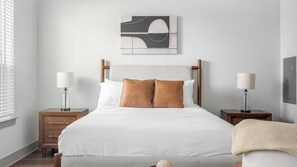 Ein Schlafzimmer mit einem Bett, zwei Nachttischen, einer Lampe, einer Decke und einem Wandbild.