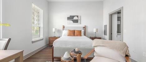 A bedroom with a bed, bedside tables, a chair, a desk, a ceiling fan, and a window with blinds.