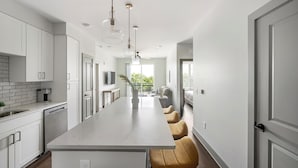 A modern kitchen with white cabinets, a central island, and pendant lighting. - Landing | Chic 2BD, Courtyard, Gym (Nashville)