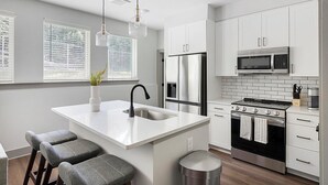 A modern kitchen with a central island, stainless steel appliances, and white cabinetry. - Landing | Chic 2BD, Courtyard, Gym (Nashville)