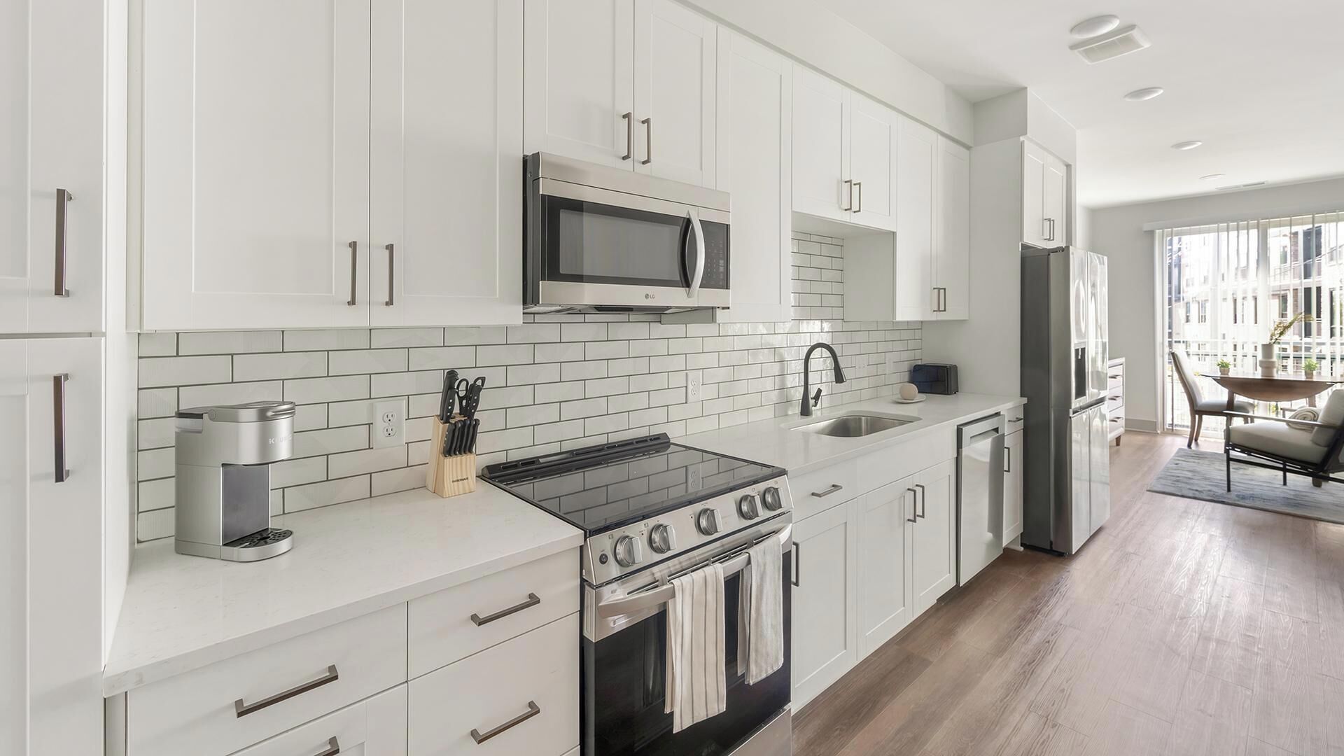 A modern kitchen with white cabinets, a stainless steel stove, a microwave, and a sink.
