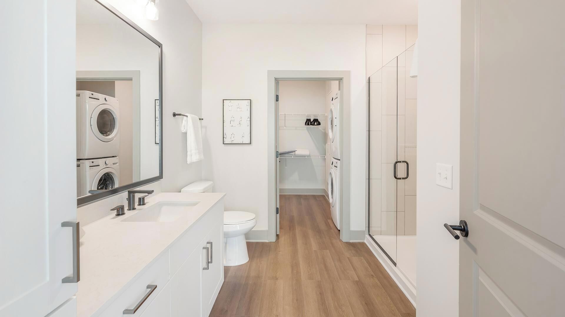 Un bany modern amb un mirall gran, un lavabo, un vàter i una màquina de rentar.