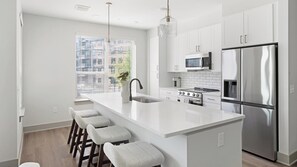 A modern kitchen with white cabinetry, a stainless steel refrigerator, a built-in oven, a microwave, and a large island with bar stools. - Landing | Spectacular 2BD, Gym, Yoga Studio (Nashville)