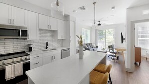 A modern kitchen with white cabinets, a black stove, and a large island. - Landing | Stylish 1BD, Courtyard, Gym (Nashville)