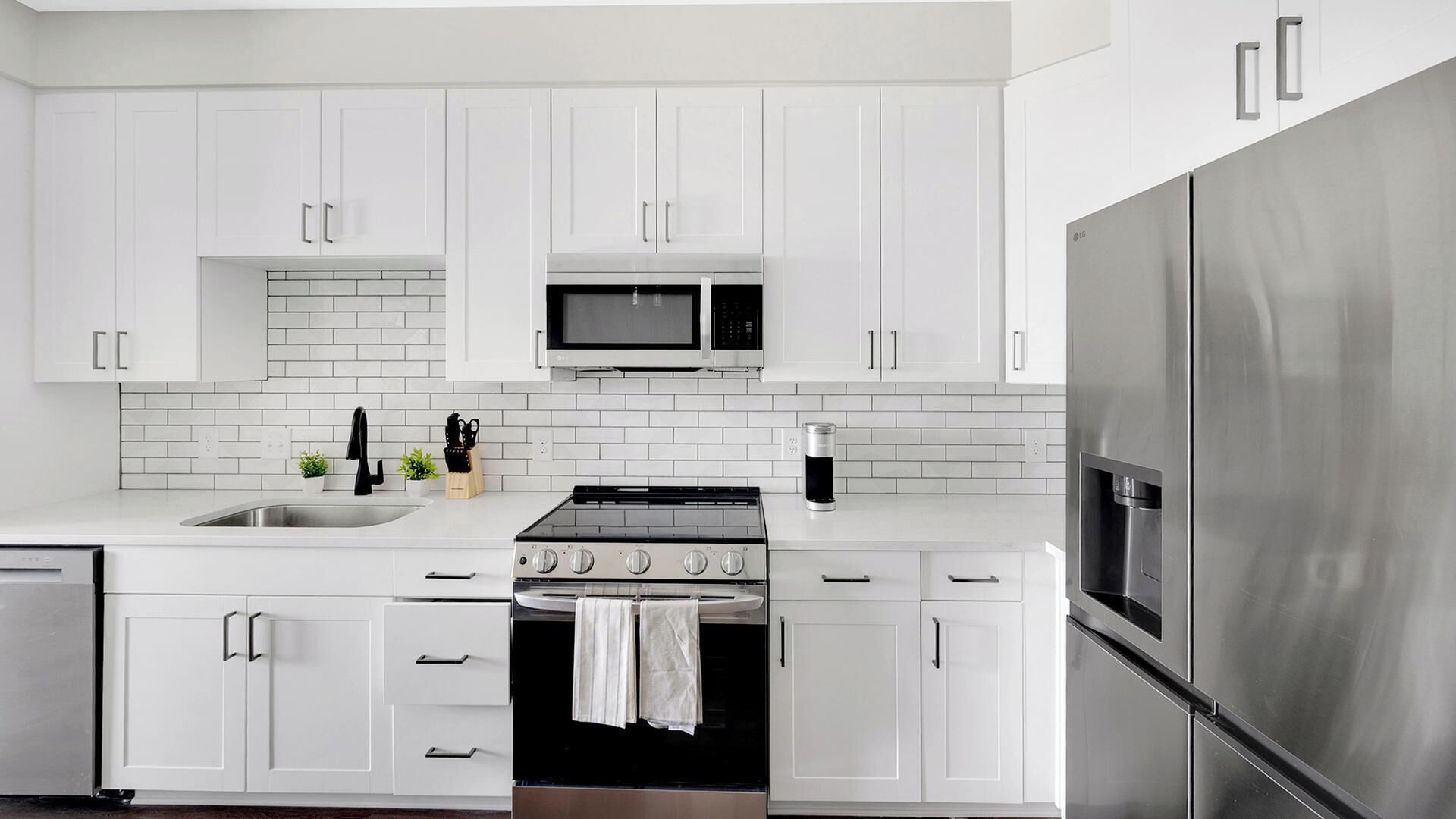 Une cuisine moderne avec des meubles blancs, un réfrigérateur en acier inoxydable, un four à micro-ondes, un four traditionnel et un évier.