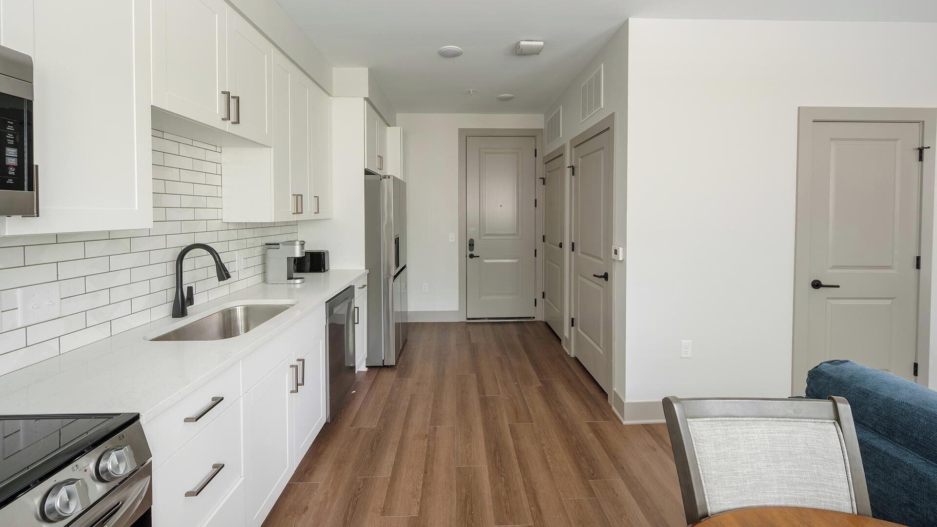 A modern kitchen with white cabinets, stainless steel appliances, and a wooden floor.