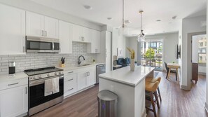 A modern kitchen with white cabinetry, a built-in microwave, a stove, and a sink. - Landing | Spectacular 1BD, Yoga Studio, Gym (Nashville)